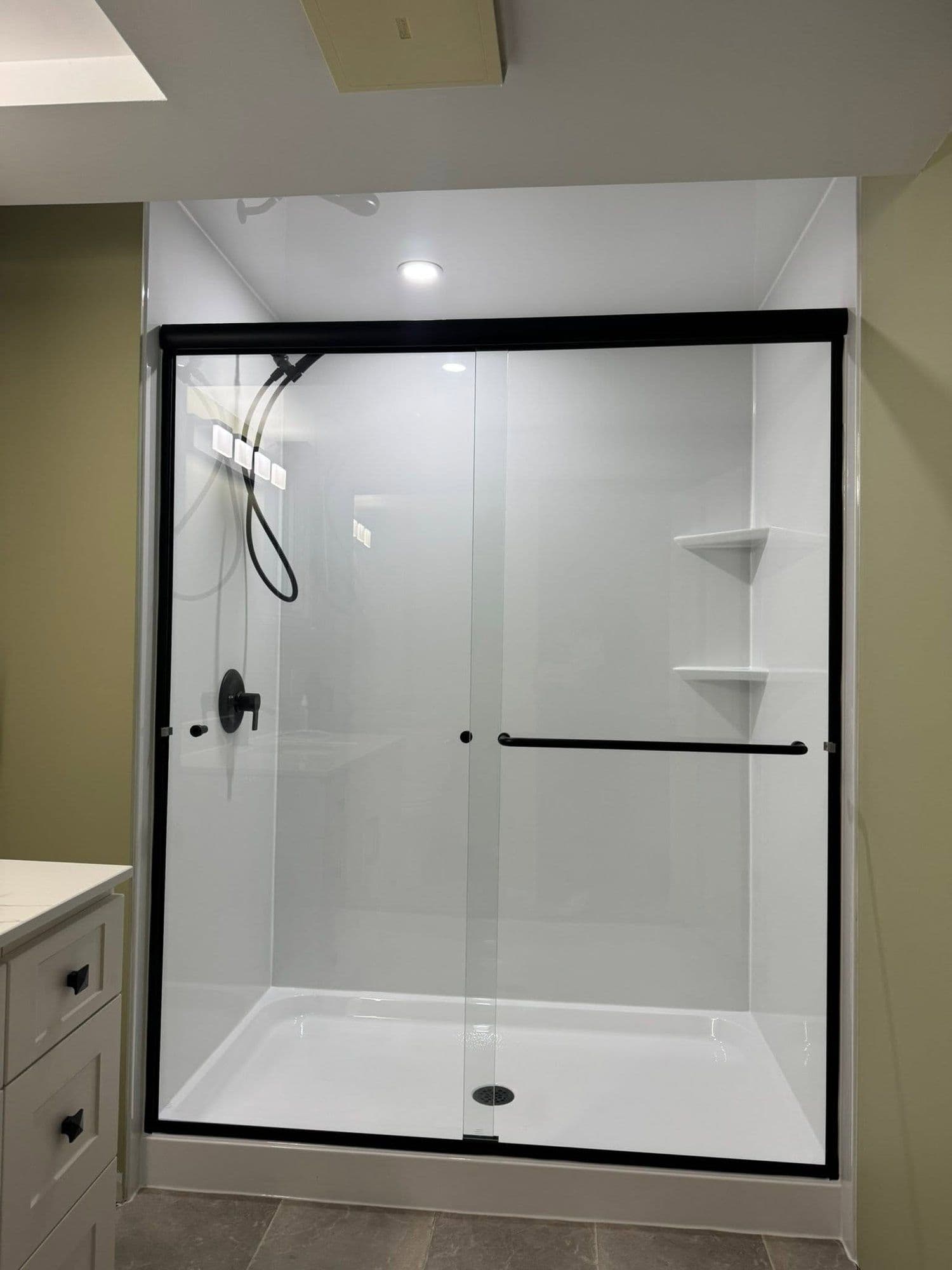 Glass shower with white surround beside a shaker vanity